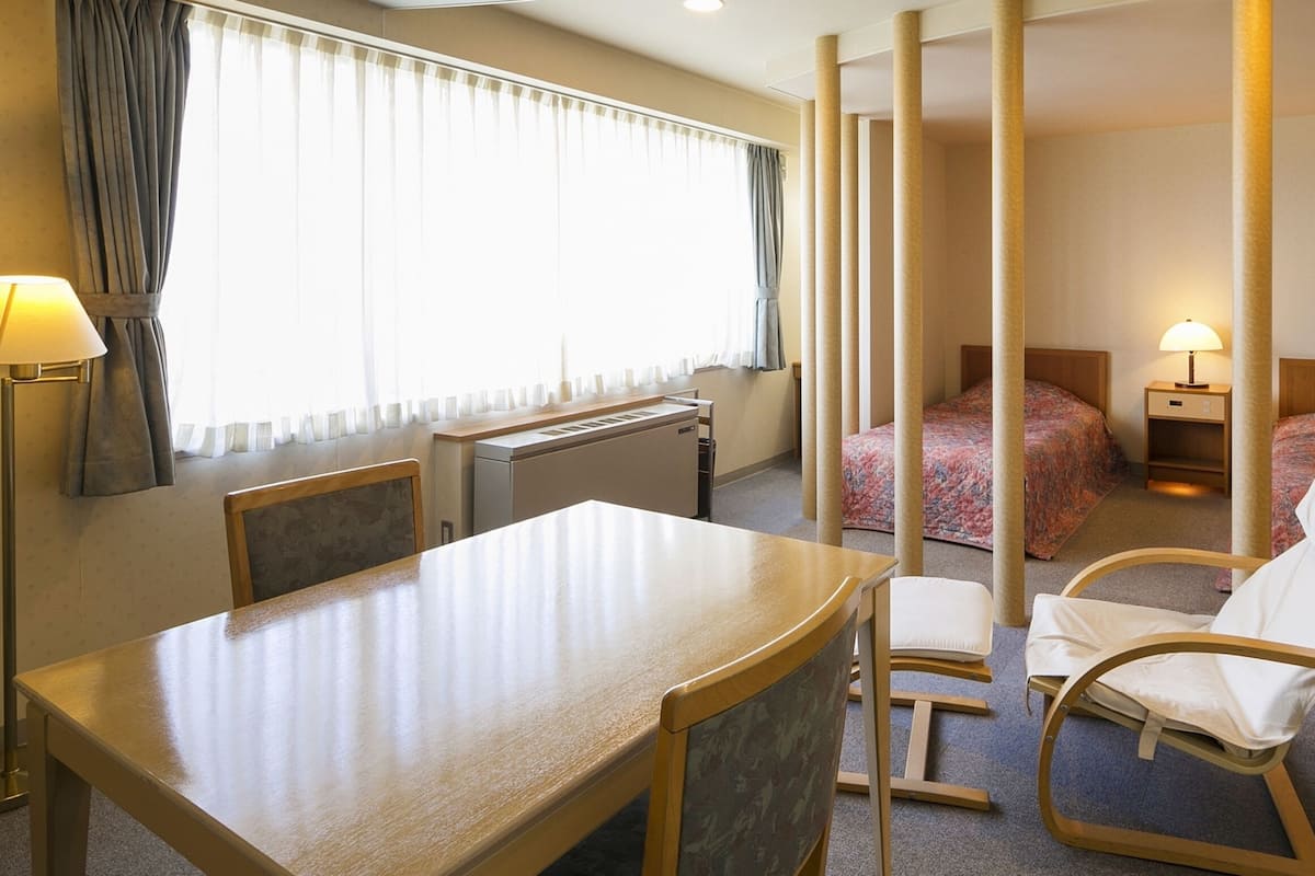 A hotel room with a dining table, two beds, a desk, and a chair.