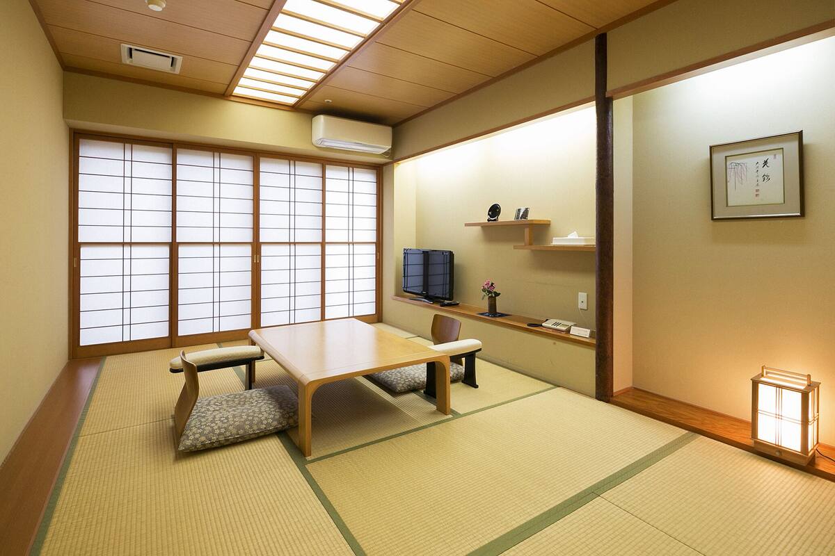 A traditional Japanese room with tatami flooring, a low table, a cushioned bench, and sliding shoji doors.