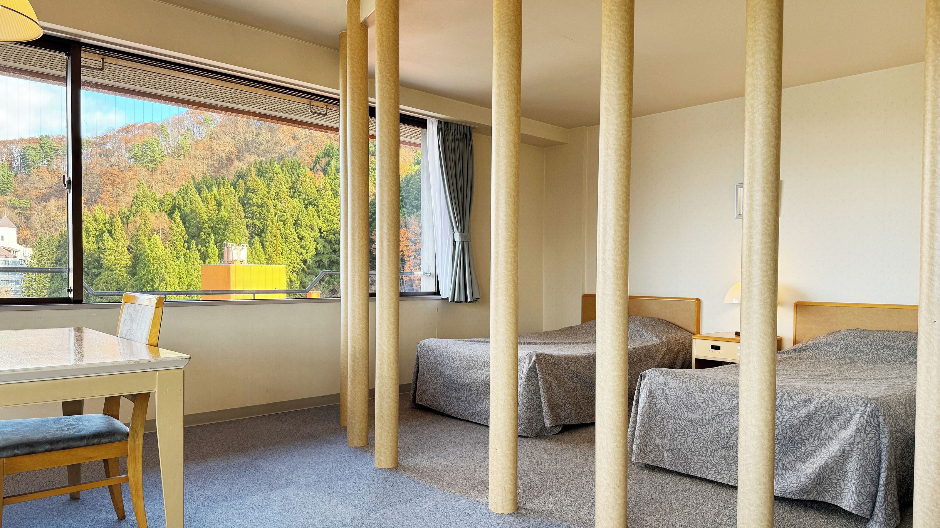 Habitación de hotel con dos camas, un escritorio y una ventana que da a vistas de árboles y edificios.