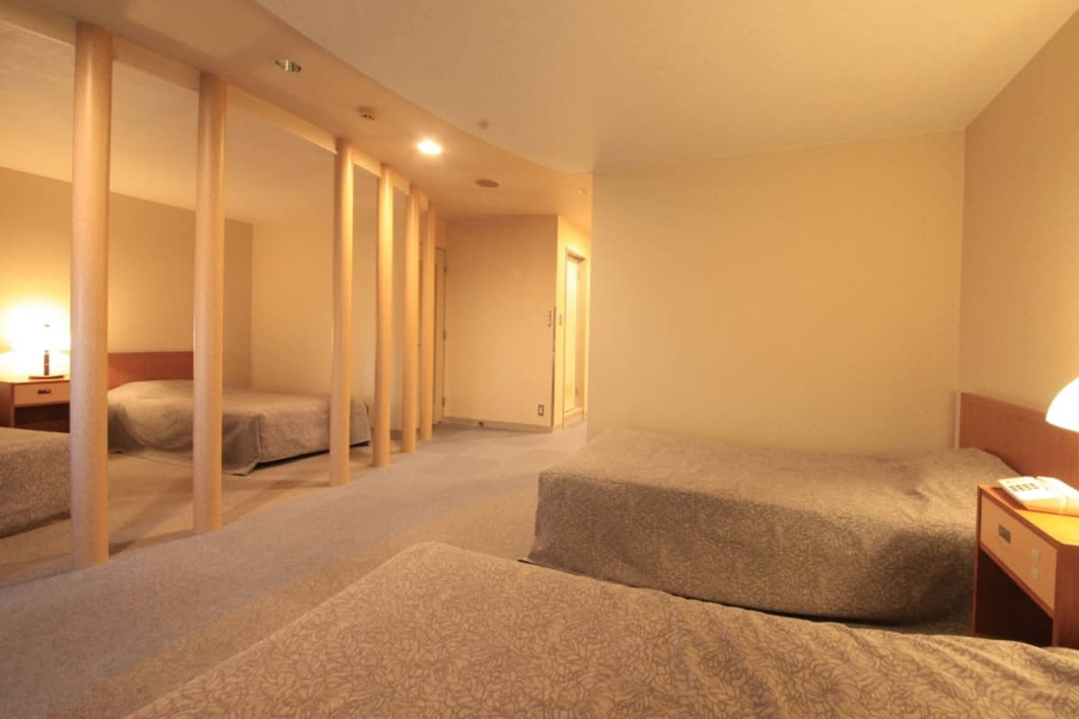 A hotel room with three single beds, a wooden partition, a desk with a lamp, and a framed picture on the wall.