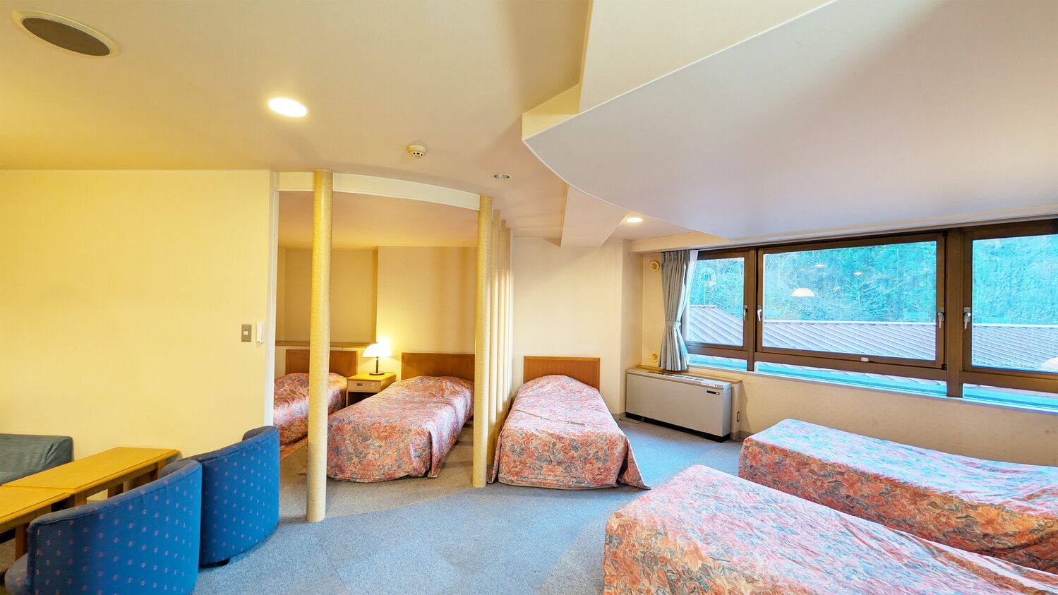 A hotel room with three beds, a sofa, a small table, and a window with a view.