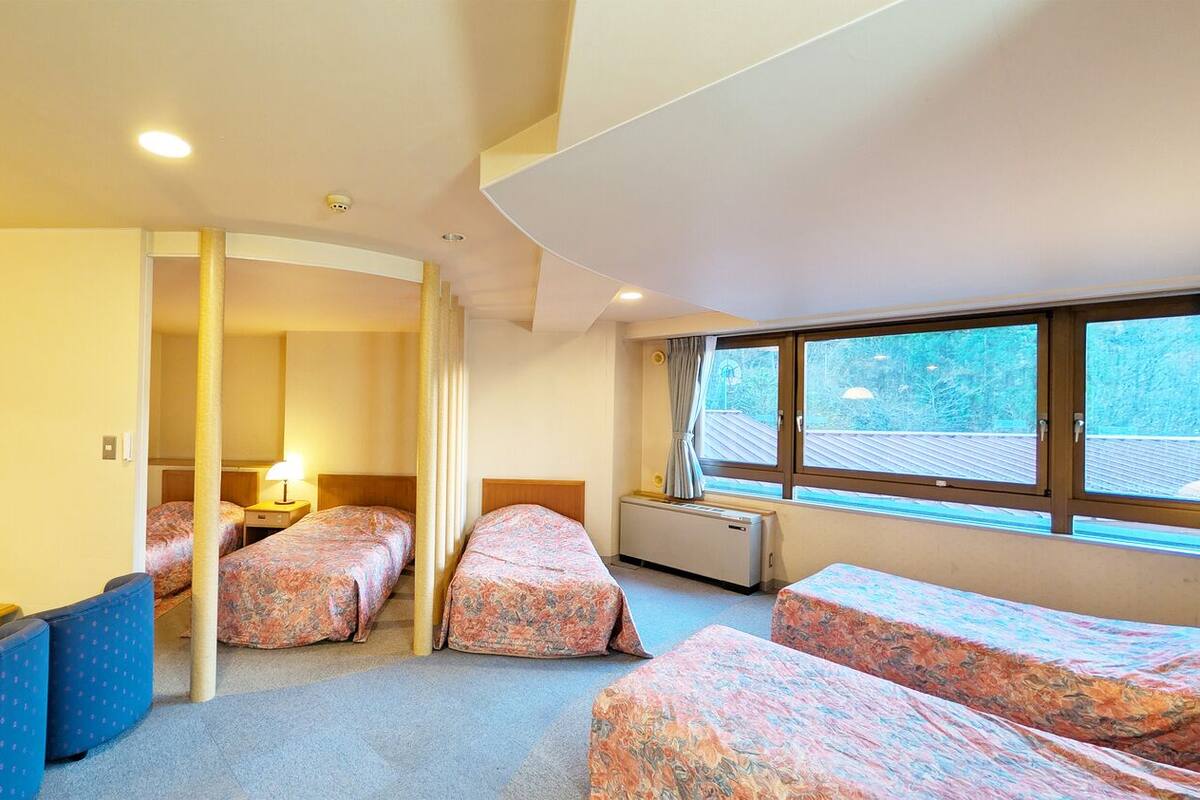 A hotel room with three beds, a sofa, a small table, and a window with a view.