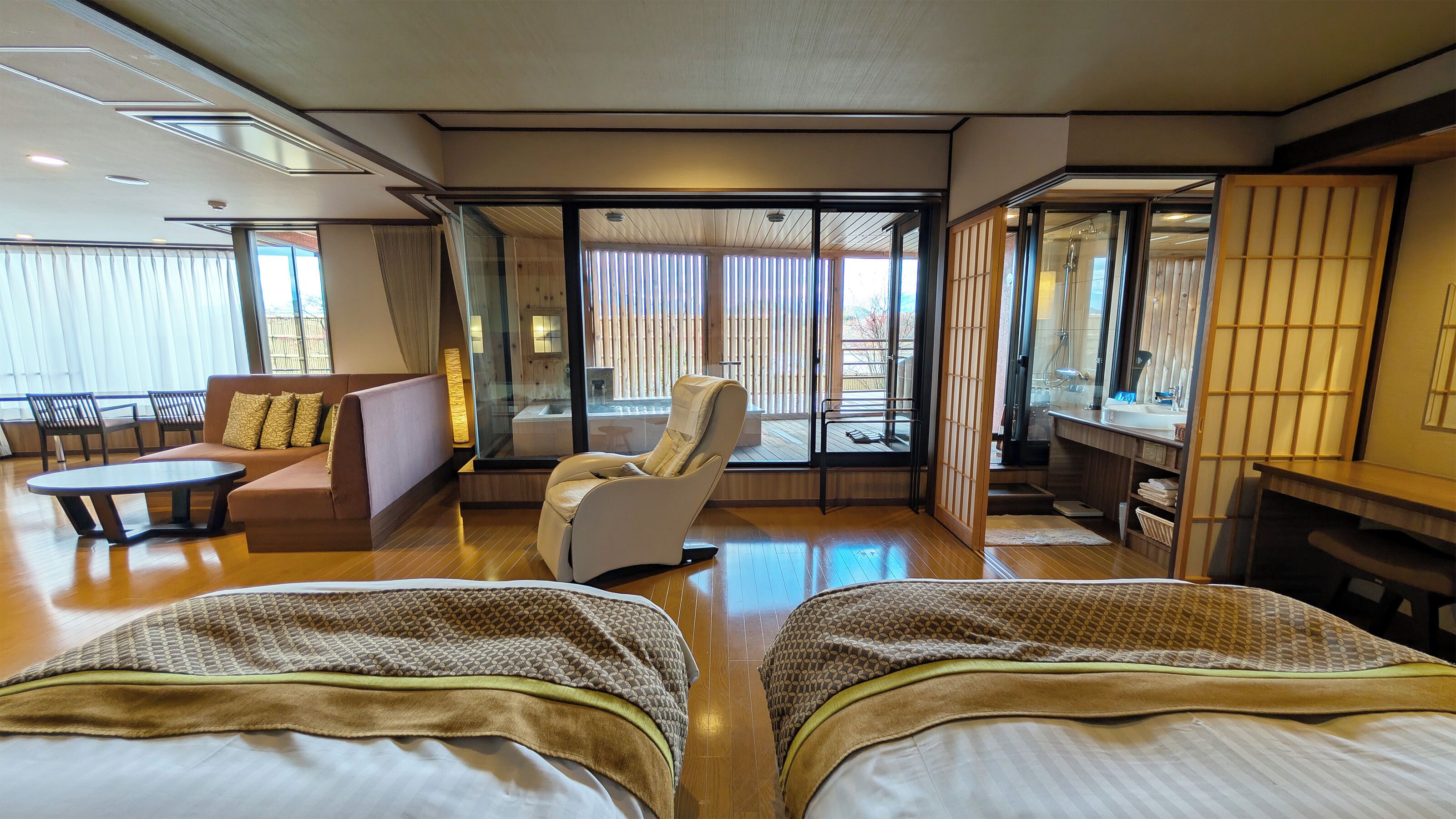 Habitación de hotel con sofá, sillón, dos camas, escritorio y puerta corrediza de vidrio a un balcón.