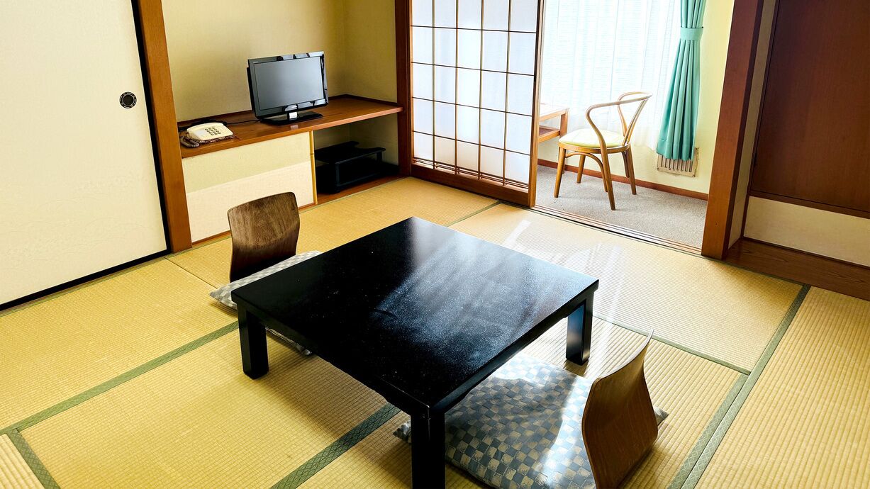 A traditional Japanese room with tatami flooring, a black table, a television, and a sliding door.