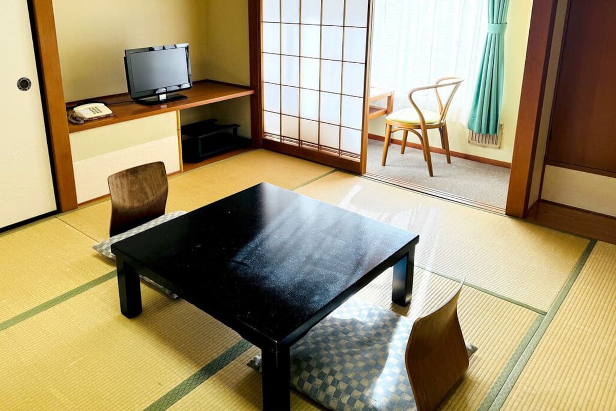 A traditional Japanese room with tatami flooring, a black table, a television, and a sliding door.