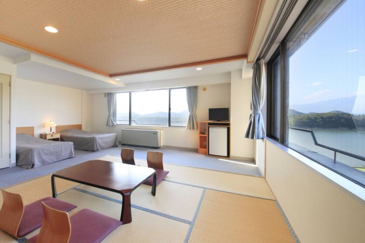 A hotel room with a bed, a desk, a chair, a TV, and a view of the outdoors.