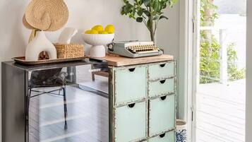 A room with a glass door leading to a balcony, a vintage typewriter, a woven basket, a bowl of lemons, and a framed picture of surfboards.