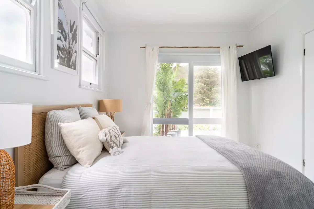 A bedroom with a bed, a TV, a window with curtains, and a view of greenery outside.