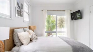 Un dormitorio con cama, televisor, ventana con cortinas y vistas a la vegetación.