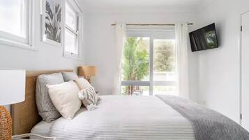 A bedroom with a bed, a TV, a window with curtains, and a view of greenery outside.