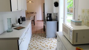A compact kitchen with white cabinets, a coffee maker, a microwave, and a window with a view of greenery. - Maison Spacieuse sur le Bassin D'arcachon (Lanton)