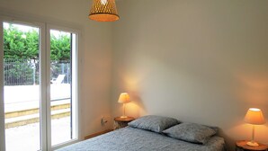 A bedroom with a bed, two bedside lamps, a hanging light fixture, and a sliding glass door leading to an outdoor area. - Maison Spacieuse sur le Bassin D'arcachon (Lanton)