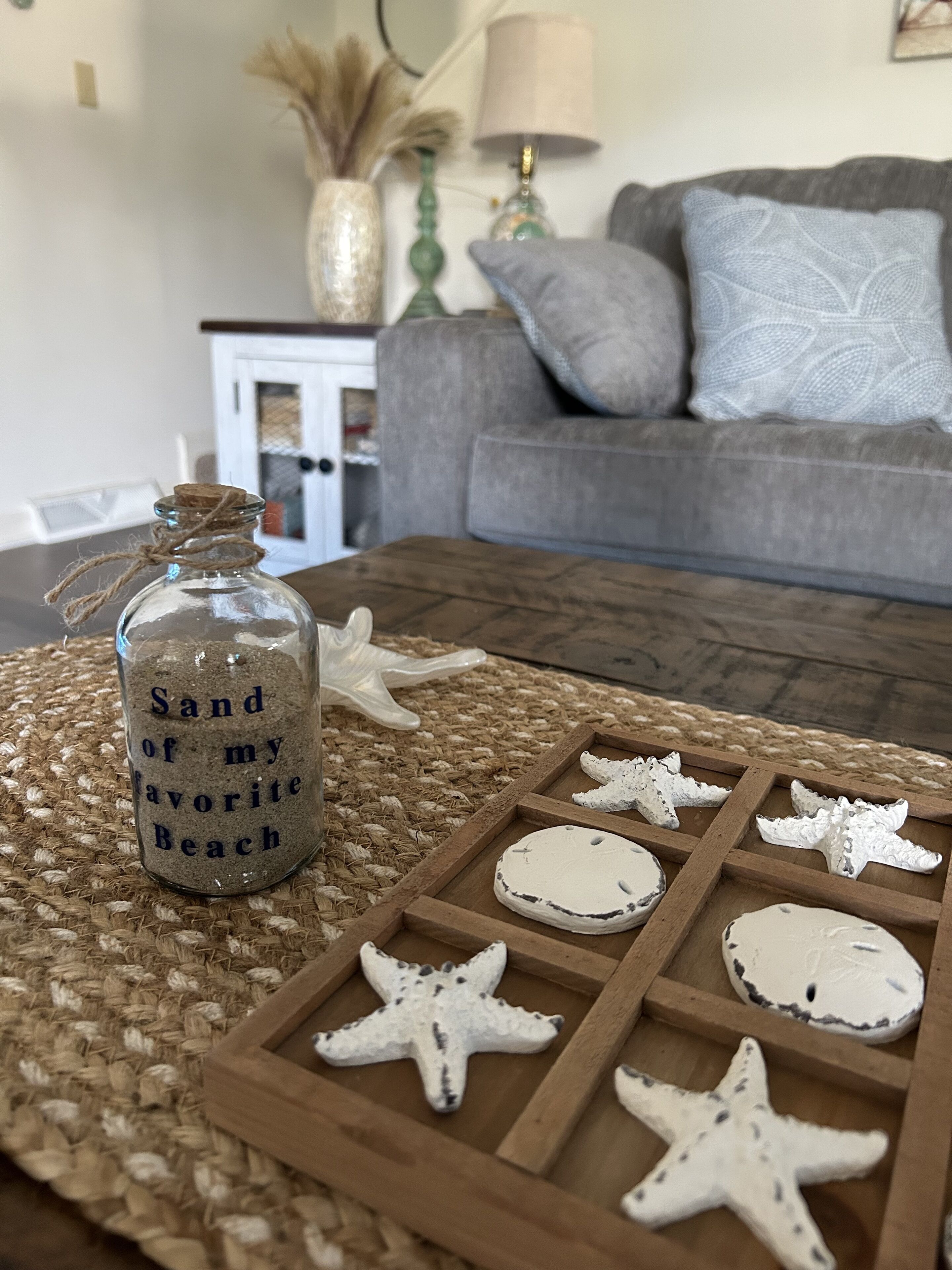 A glass bottle labeled "Sand of my favorite Beach" on a woven placemat, surrounded by starfish-shaped cookies on a wooden tray.