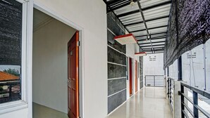 A hallway with a tiled floor, a red door, and a metal railing. - Super OYO 3702 Homestay Bougenville Syariah (Lamongan)