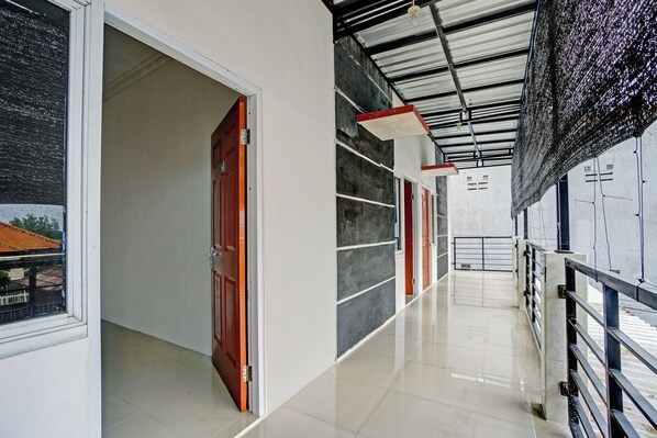A hallway with a tiled floor, a red door, and a metal railing.
