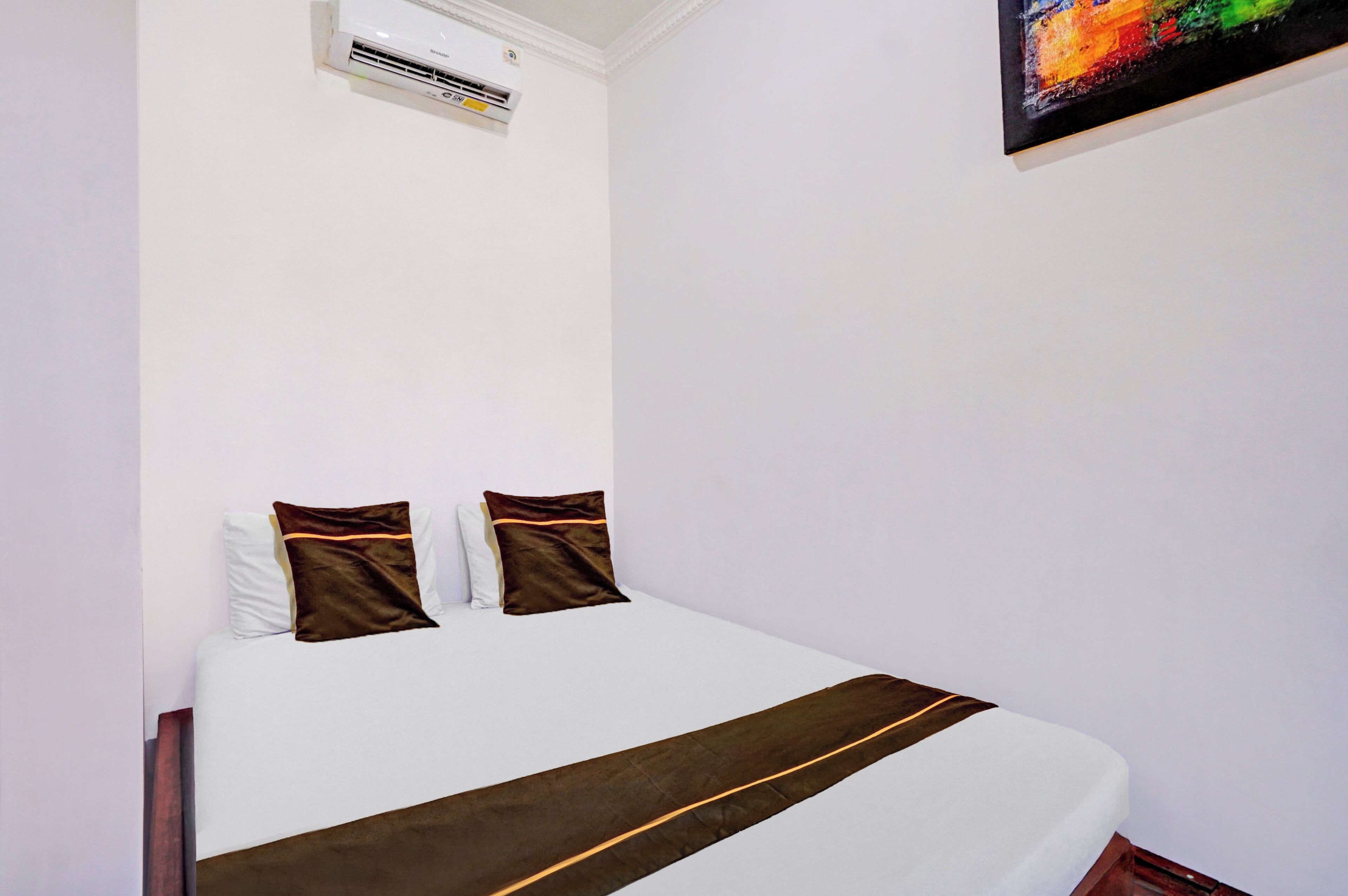 Une chambre d’hôtel avec un lit, des oreillers, une couverture, un appareil de climatisation et un tableau au mur.