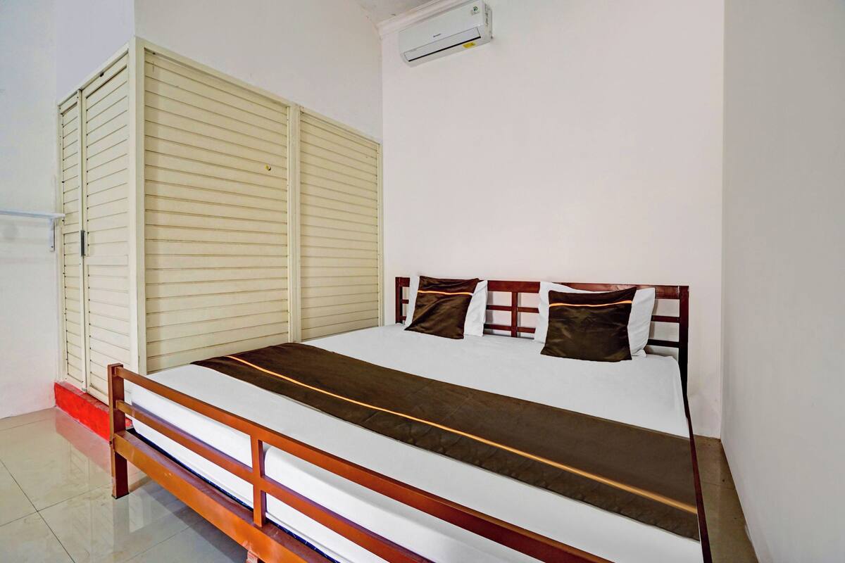 Una cama individual con estructura de madera, colchón blanco y cabecera marrón.