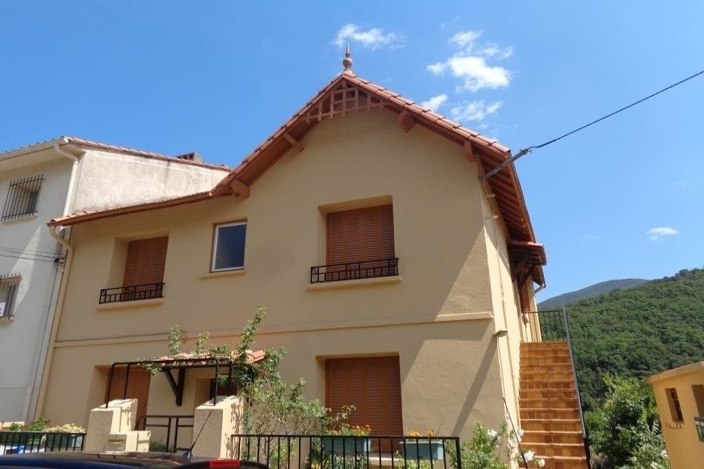 A two-story building with a tiled roof, multiple windows with shutters, and a small balcony.