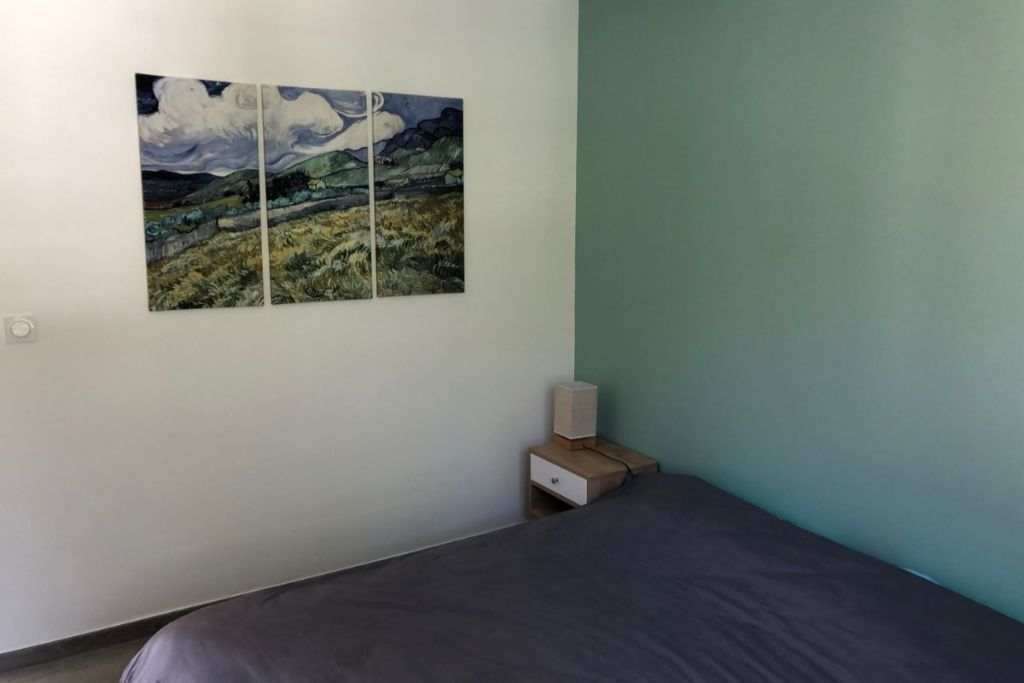 Une chambre à coucher avec un lit, une table de chevet dotée d’un haut-parleur et un tableau accroché au mur.