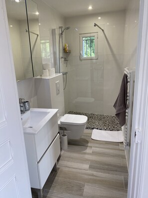 Ein modernes Badezimmer mit Duschkabine aus Glas, Toilette in Weiß, Waschbecken mit Spiegel und kleinem Fenster für Tageslicht.