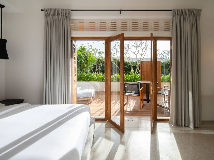 A hotel room with a bed, a desk, and a view of a garden through a sliding glass door.