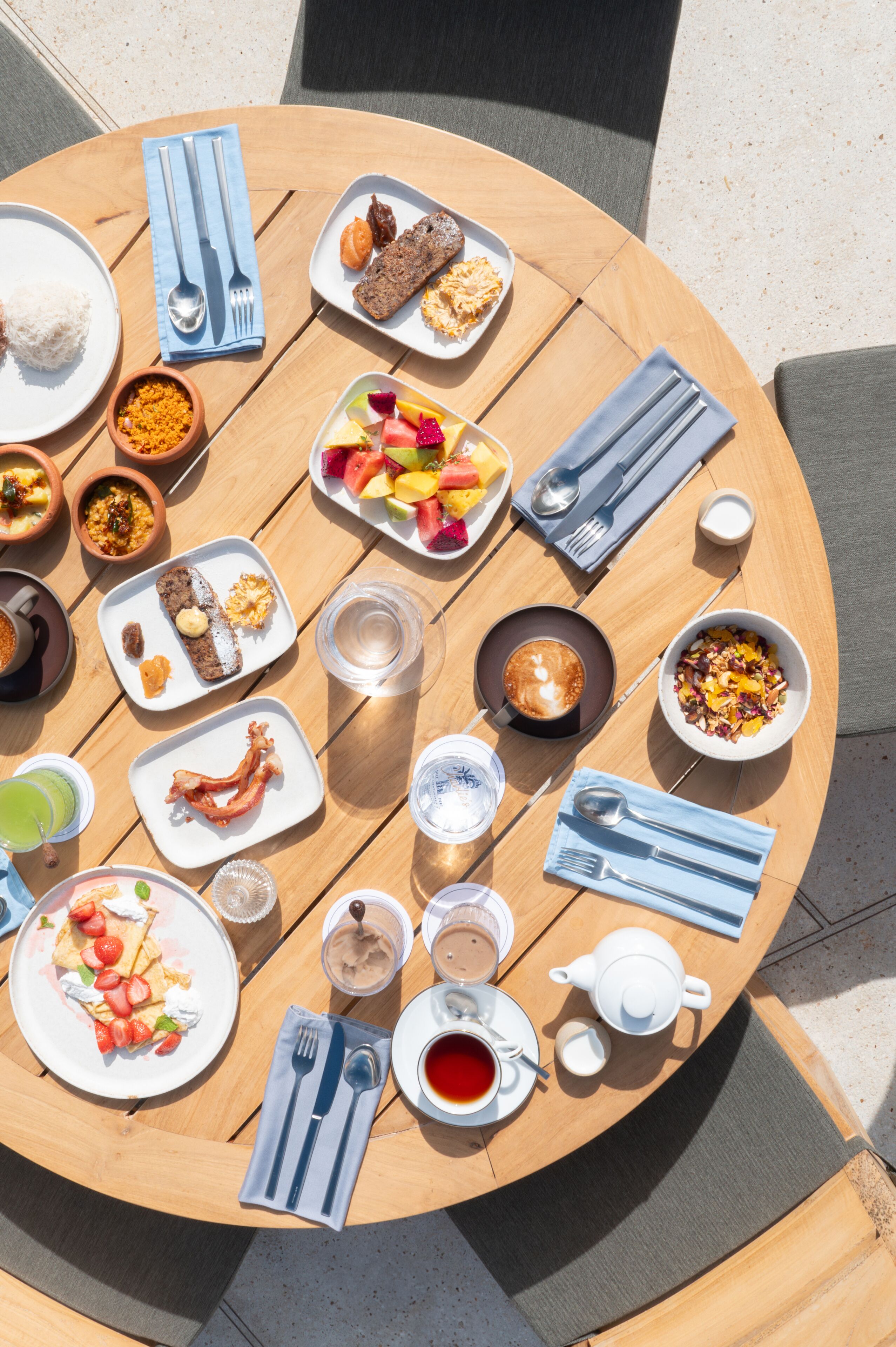 Una mesa redonda de madera con diversos alimentos para el desayuno, incluyendo platos de comida, tazas de café y una tetera.
