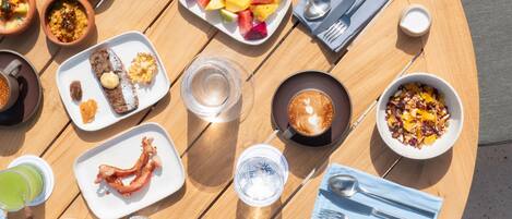 Una mesa redonda de madera con diversos alimentos para el desayuno, incluyendo platos de comida, tazas de café y una tetera.