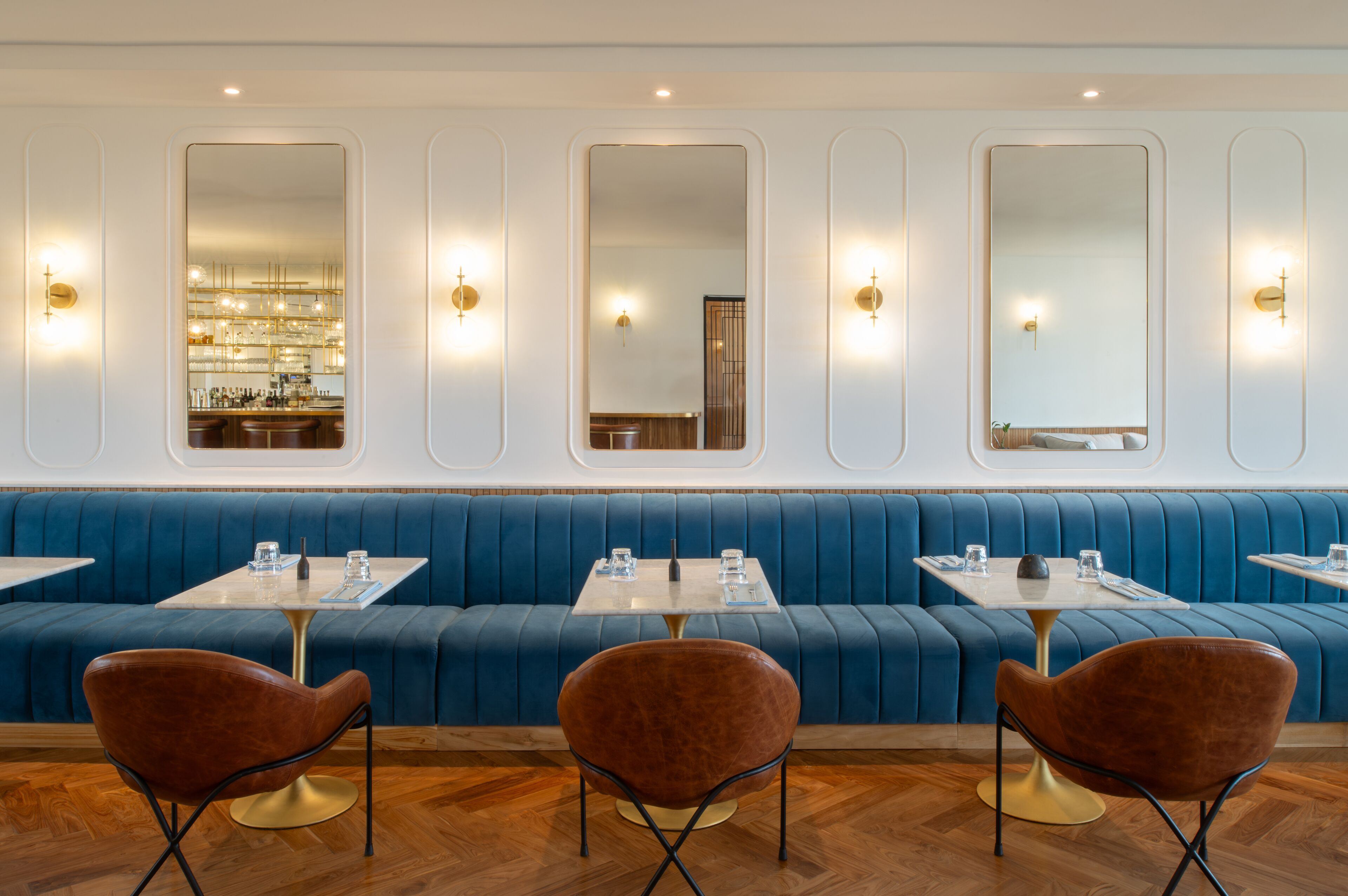 A modern restaurant interior with blue upholstered booths, round tables, and brown chairs.