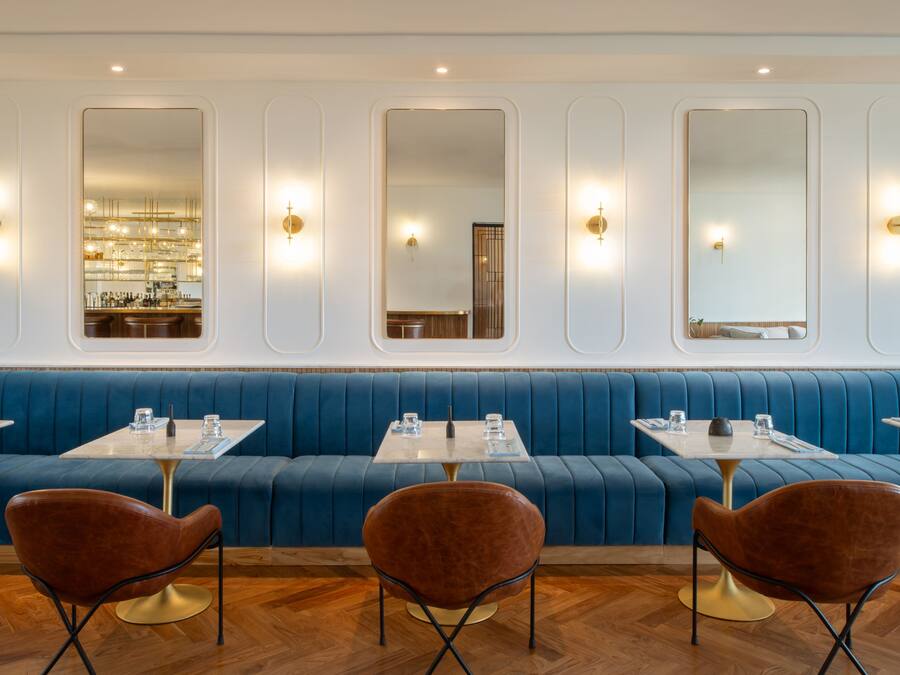 Un interior de restaurante moderno con asientos tapizados en azul, mesas redondas y sillas marrones.