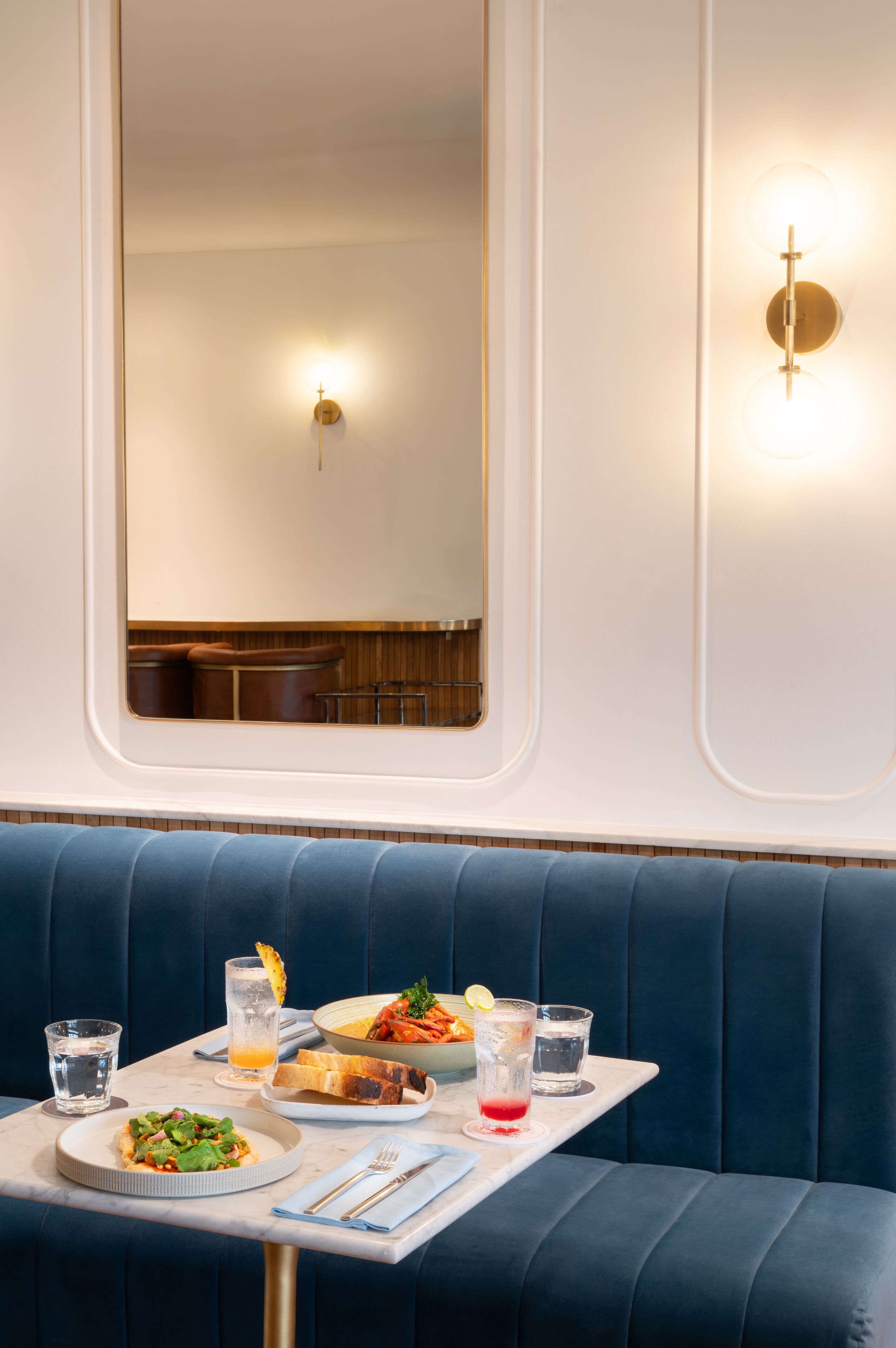 Un comedor con una mesa dispuesta para dos personas, incluyendo platos de comida, vasos y cubiertos.
