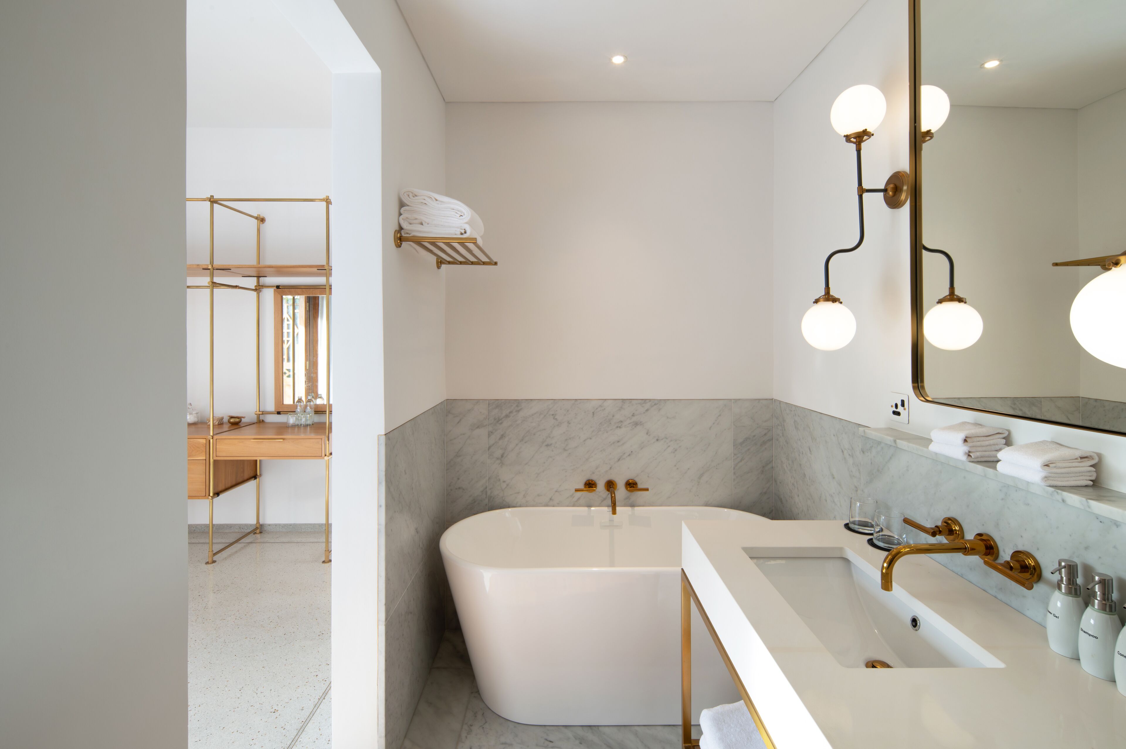 Un baño moderno con una bañera independiente, un tocador con grifo dorado y un espejo grande con luces redondas.