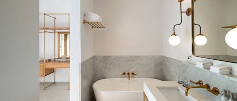 Un baño moderno con una bañera independiente, un tocador con grifo dorado y un espejo grande con luces redondas.
