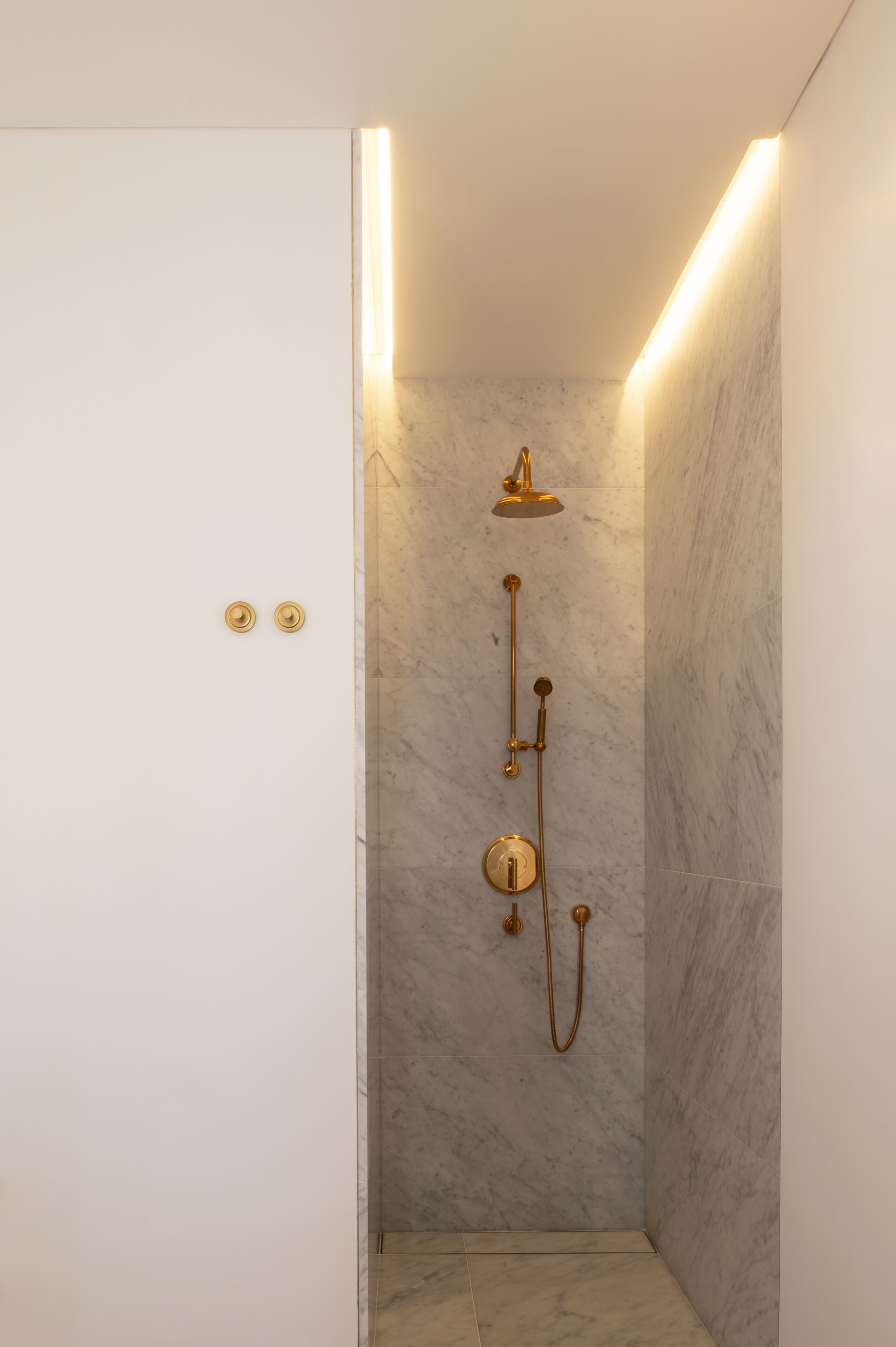 A shower with a gold fixture, marble walls, and a light strip on the ceiling.