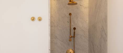A shower with a gold fixture, marble walls, and a light strip on the ceiling.