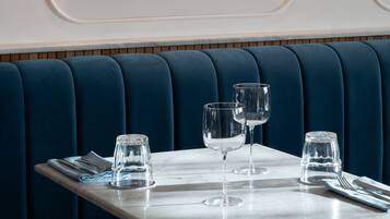 Un comedor con una mesa dispuesta para dos personas, un asiento tapizado azul y un espejo montado en la pared.