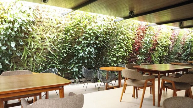 An indoor seating area with tables and chairs, surrounded by a variety of green plants. - Gosyen Azana Hotel Salatiga (Salatiga)