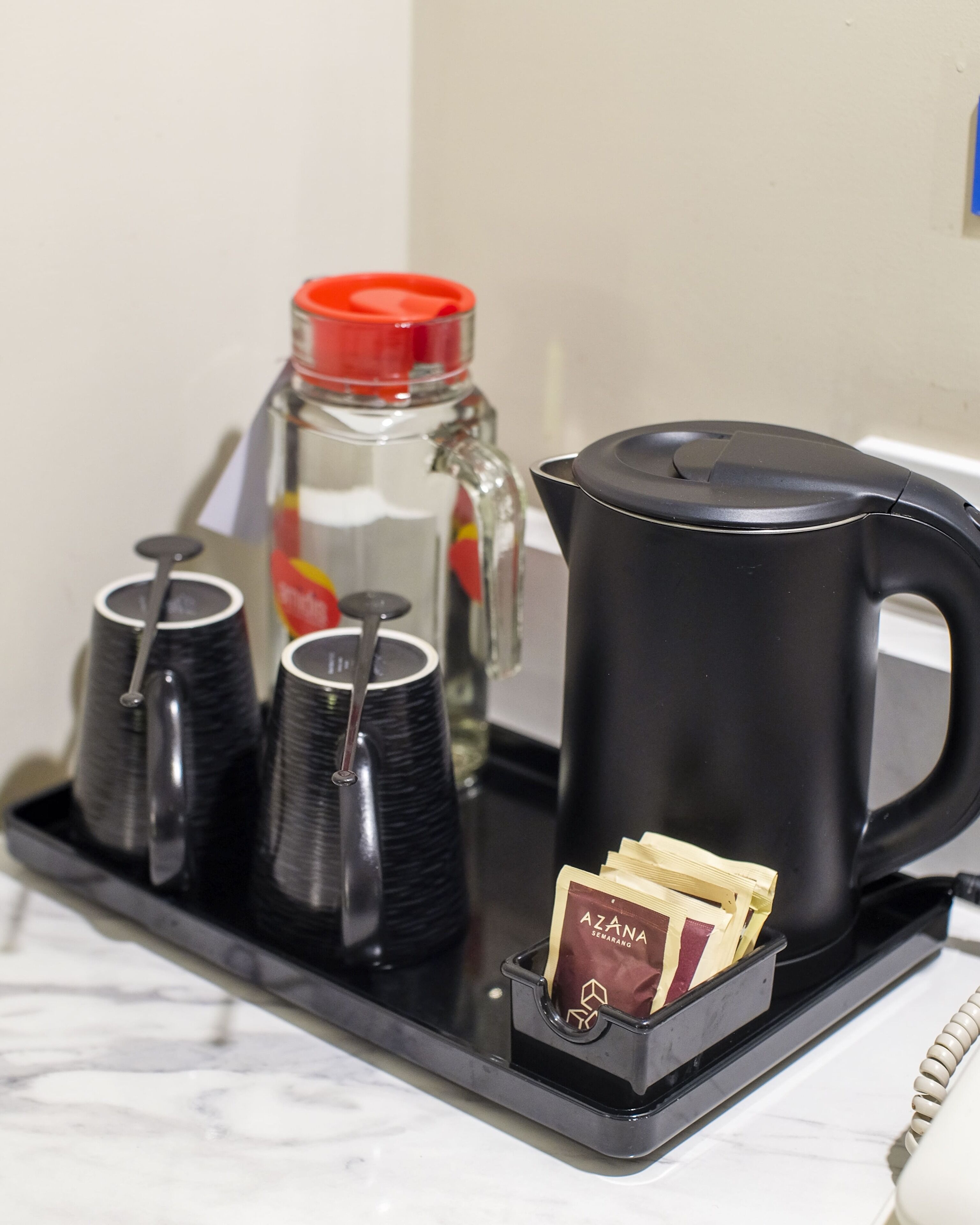 Uma bandeja com uma cafeteira, quatro xícaras, uma garrafa e um sachê de chá.