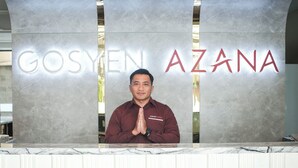 A reception desk with a marble counter and a man standing behind it. The words "GOSYEN AZANA" are visible on the wall behind the desk. - Gosyen Azana Hotel Salatiga (Salatiga)