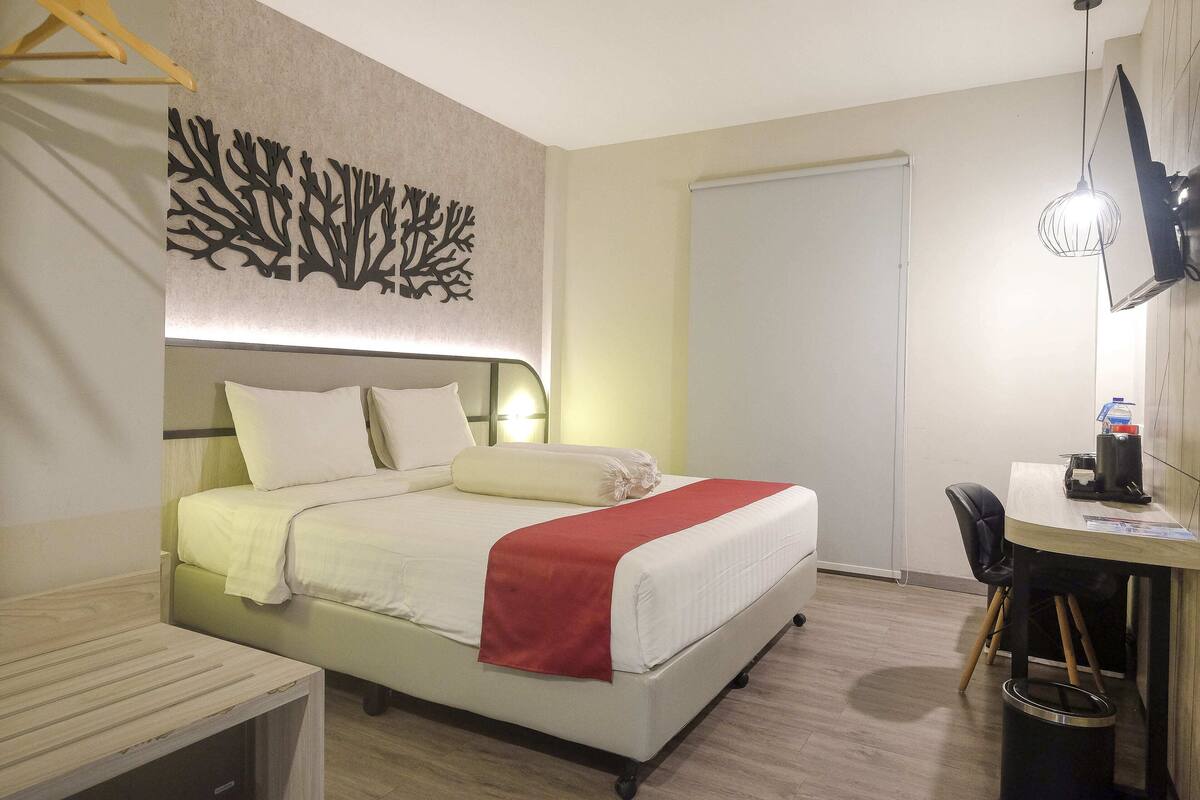 A modern hotel room with a neatly made bed, a desk with a chair, and a wall-mounted TV.