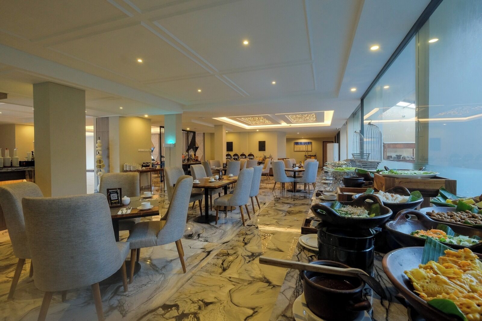 A spacious dining area with marble flooring, multiple tables and chairs, and a buffet with various dishes.