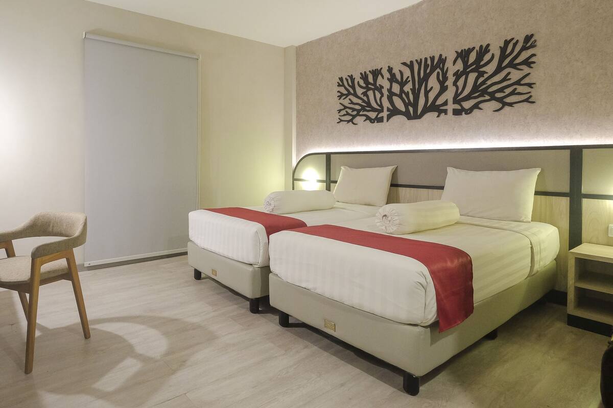 A hotel room with two beds, a chair, and a wall-mounted artwork.