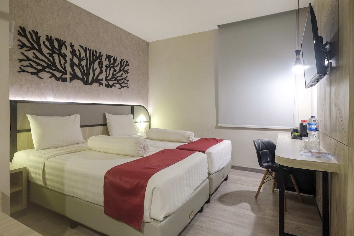 A hotel room with two beds, a desk, a chair, a TV, and a wall art piece.
