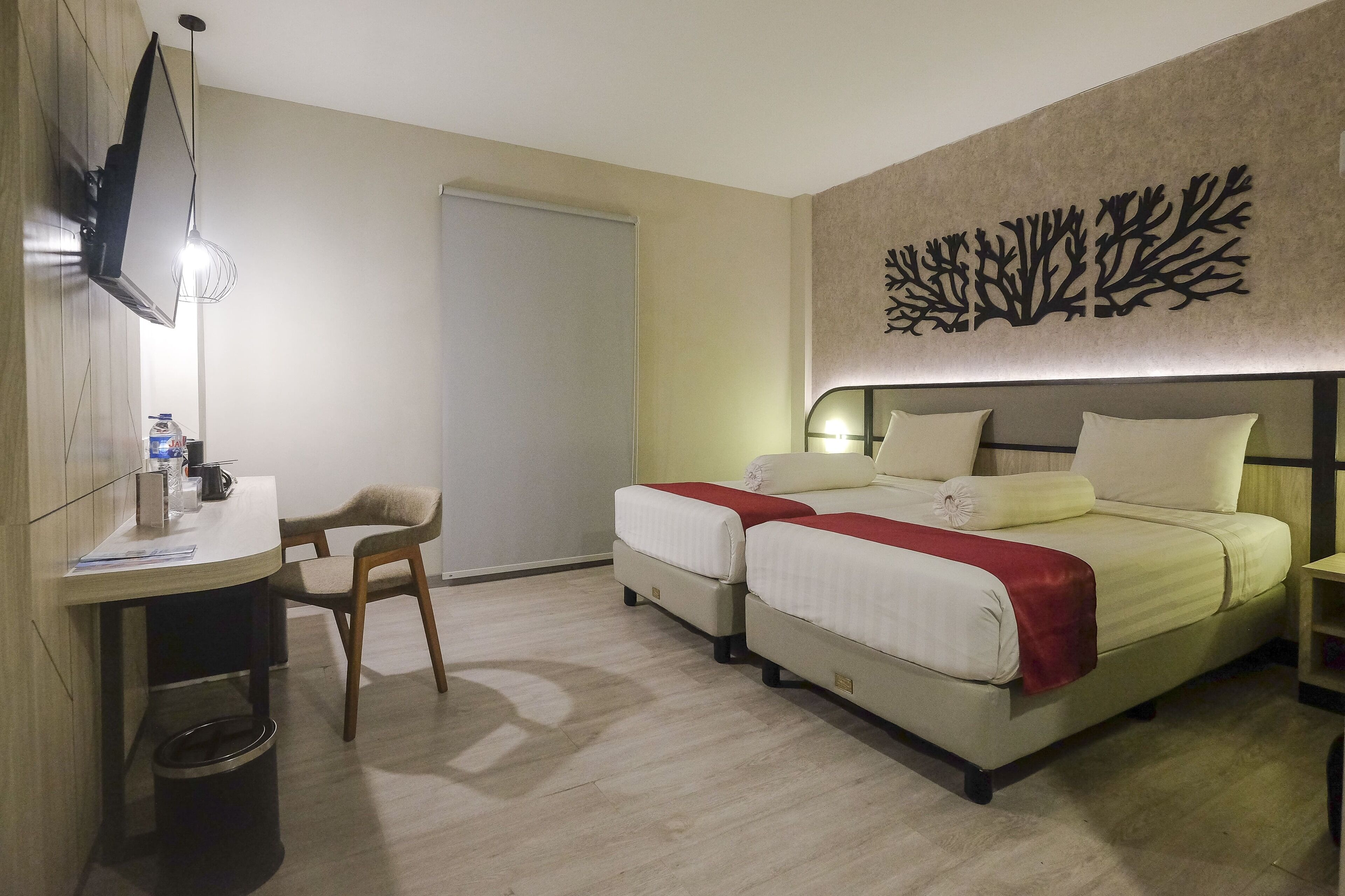 A hotel room with two beds, a desk, a chair, a TV, and a wall decoration.