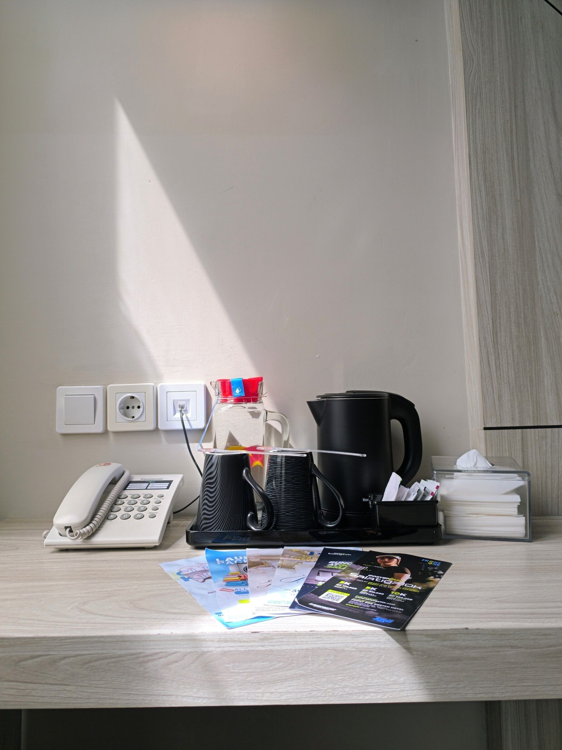 A desk with a telephone, a coffee maker, a kettle, and a tissue box.
