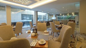 A modern dining area with high ceilings, large windows, and a view of the cityscape. - Gosyen Azana Hotel Salatiga (Salatiga)