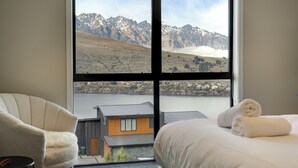 Een hotelkamer met een groot raam met uitzicht op de bergen, een bed met een opgerolde handdoek en een stoel.