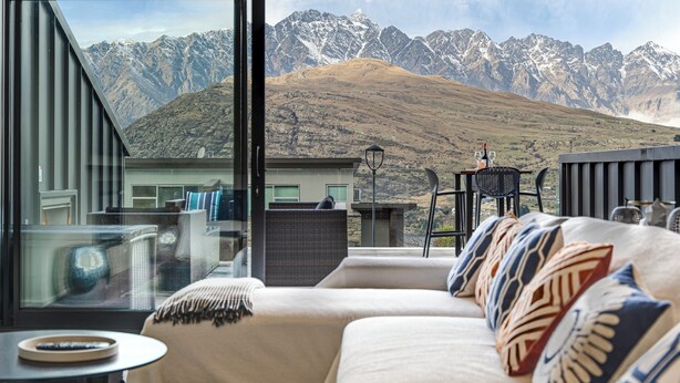 Een moderne woonkamer met een bank, een glazen tafel en uitzicht op besneeuwde bergtoppen.