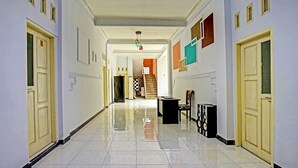 Un largo pasillo estrecho con paredes blancas y un piso de baldosas brillantes. Hay puertas a ambos lados, una escalera al final y una pequeña mesa con sillas en el centro.