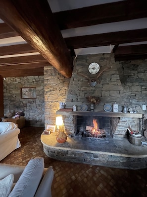A stone fireplace with a lit fire, a clock, and a small shelf with decorative items.