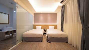 A hotel room with two beds, a bathroom, and a large window with curtains.